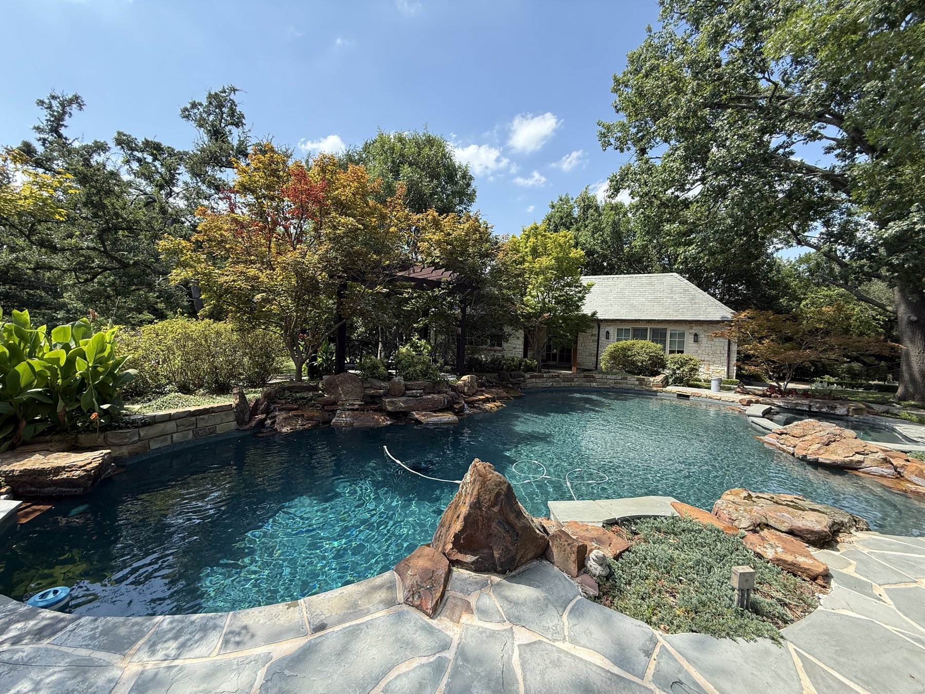 Natural stone lagoon-style backyard pool with waterfall feature serviced by The Texas Pool Company
