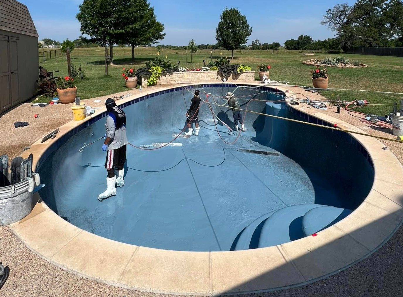 Crew spray-applying Midnight Blue pebble finish to a pool