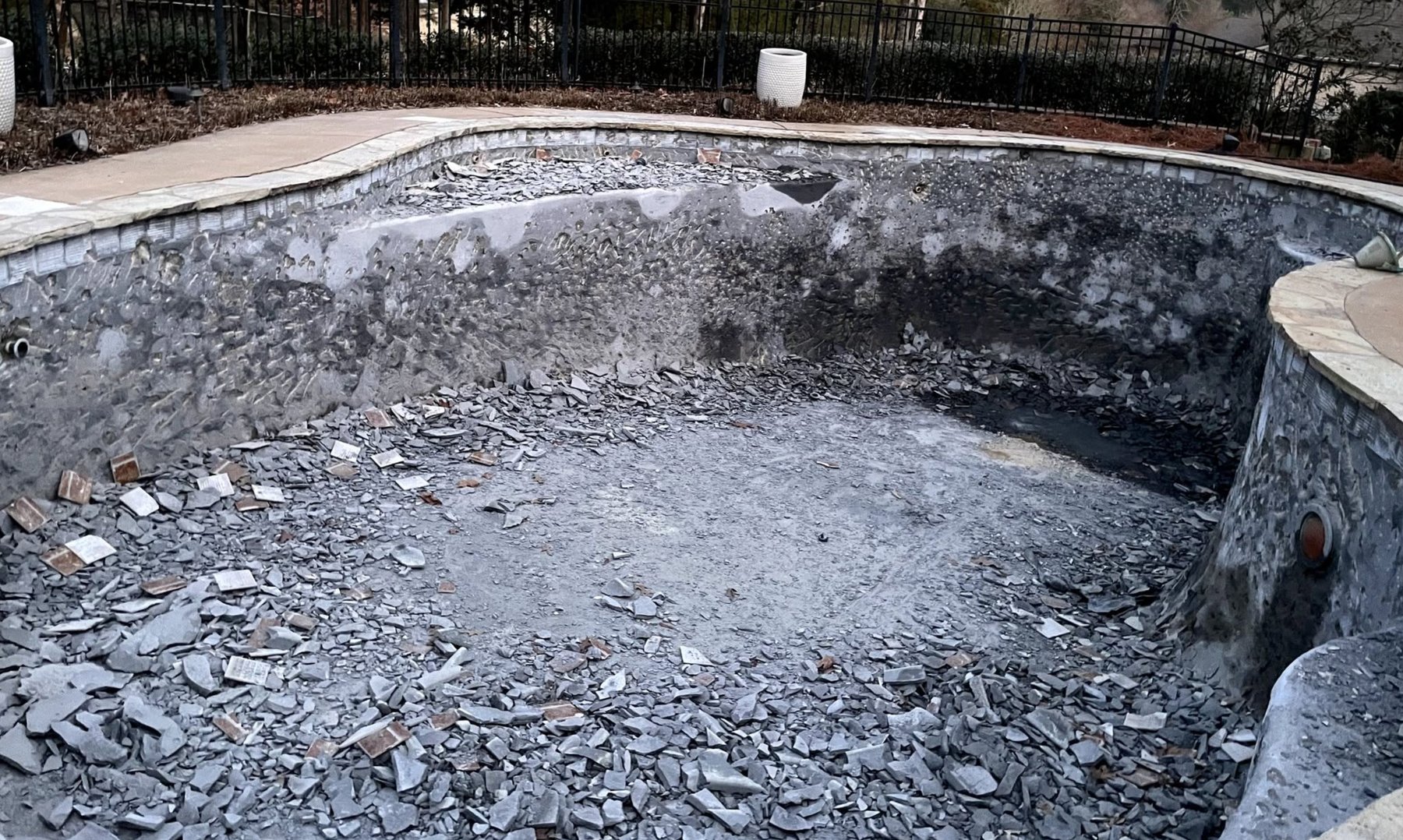 Drained pool with old plaster chipped away and demolished during a resurfacing remodel