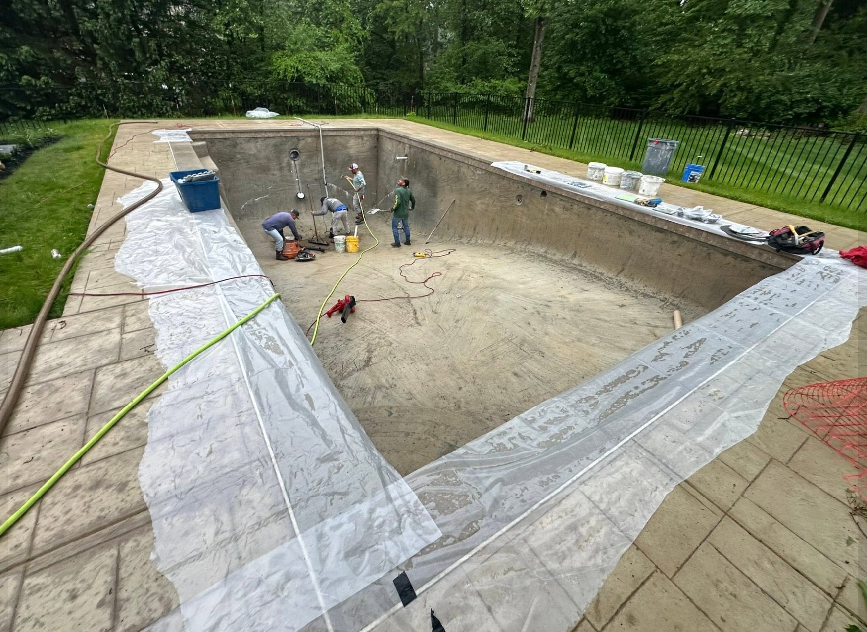 Pool before resurfacing, drained with crew prepping the surface for new plaster