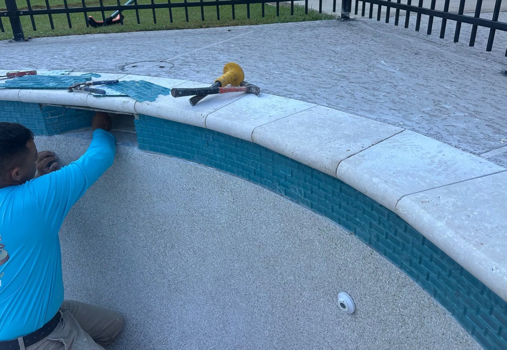 Technician installing new waterline tile and coping on a pool during a remodel